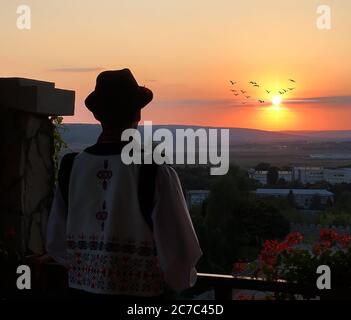 Plan horizontal d'un homme dans des vêtements traditionnels moldaves regardant le coucher du soleil au loin Banque D'Images