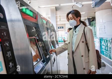 Jeune femme portant un masque dans la station de métro pour utiliser des machines automatiques Banque D'Images