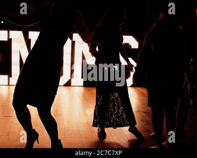 Photo sombre de deux femmes dansant en silhouette sur un fête avec des lumières en arrière-plan Banque D'Images