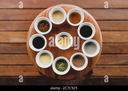 Dose au-dessus de dix bols blancs avec différentes sauces et épices en eux alignés sur un tabouret Banque D'Images