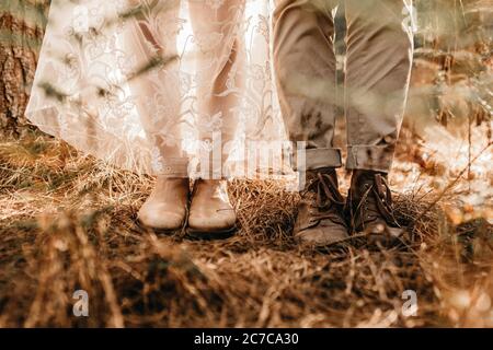 Gros plan des jambes d'une femme dans une robe blanche et des bottes blanches, et des jambes d'un homme dans des bottes brunes Banque D'Images