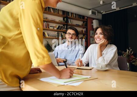 Groupe de collègues souriants assis à la réception avec ordinateur portable tout en discutant au travail dans un bureau moderne Banque D'Images