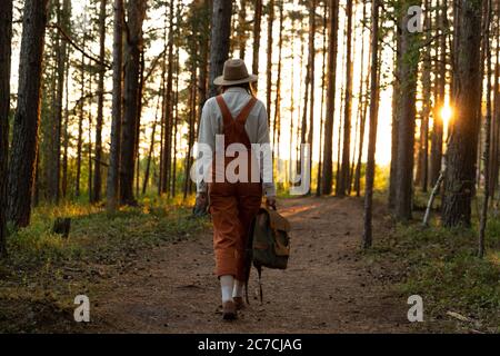 Femme botaniste en combinaison orange avec sac à dos sur sentier écologique de randonnée en forêt. Naturaliste explorant la faune et écotourisme aventure marche i Banque D'Images
