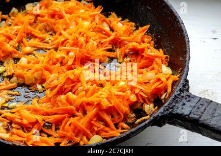 Morceaux d'oignons frits et de carottes dans une poêle. Les oignons coupés en dés et les carottes râpées sont frits sur le poêle. Cuisine. Plats faits maison. Mise au point sélective Banque D'Images