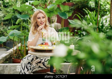 Belle jeune femme appréciant la nourriture délicieuse dans un café extérieur avec beaucoup de plantes et d'arbres autour Banque D'Images