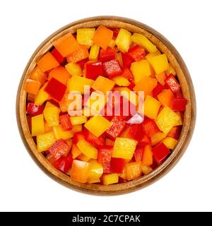 Poivrons coupés en dés dans un bol en bois. Poivron, poivron ou paprika, coupé en copeaux colorés. Fruits frais jaunes, orange et rouges. Banque D'Images