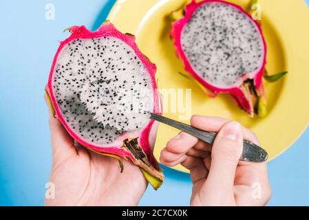 Pitaya est le fruit du dragon. La fille mange un fruit tropical avec une cuillère. pitaya douce sur fond bleu. Assiette jaune et fruits coupés Banque D'Images