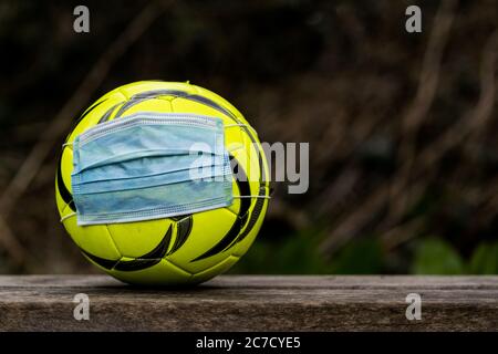 ballon de football jaune portant un masque médical. Coronavirus dans le sport, tous les événements annulés. Banque D'Images