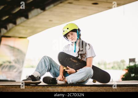 Écolière après des leçons de pratique de skateboard dans un parc de skate extérieur. Élégante et belle fille caucasienne avec skateboard sur une rampe à demi-pipe Banque D'Images