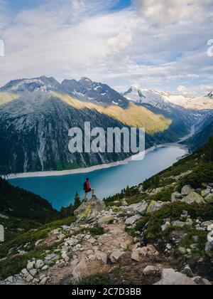 La silhouette de l'homme reste sur un pic de roche vif. Satisfaire les randonneurs profiter de la vue. Homme haut sur une falaise rocheuse regardant sur le lac bleu entouré de montagnes dans l'Al Banque D'Images