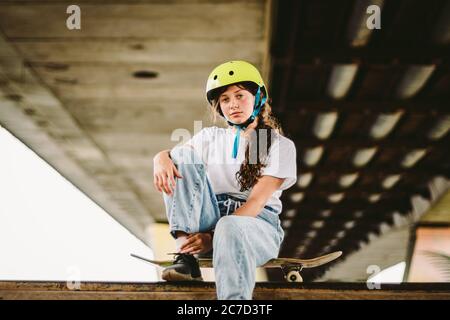 Écolière après des leçons de pratique de skateboard dans un parc de skate extérieur. Élégante et belle fille caucasienne avec skateboard sur une rampe à demi-pipe Banque D'Images