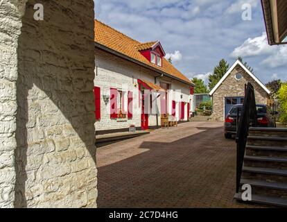 Maison blanche avec rideaux rouges et toit marron et une voiture dans la rue sous ciel nuageux Banque D'Images