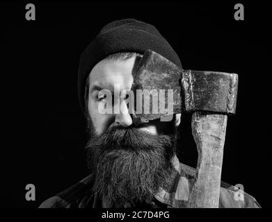 Bel homme ou bûcheron, hipster barbu avec barbe et moustache en hat détient old rusty lame de fer d'ax isolé sur fond noir Banque D'Images