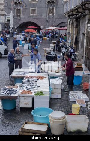 CATANE, ITALIE - 15 octobre 2016: Poisson monger nettoyage du poisson pour les clients d'attente, qui parlent à son partenaire. Marché, Catane, Sicile, Italie Banque D'Images