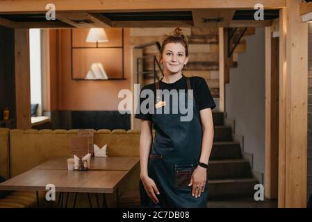 Une jeune serveuse souriante pose dans un restaurant. Un barista gentil se prépare à travailler dans un café. Banque D'Images