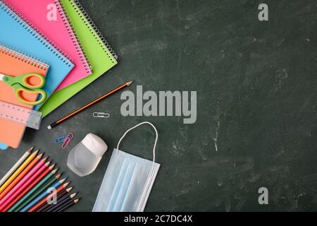 Fournitures scolaires telles que carnets, crayons de couleur et autres sur tableau noir vert avec protection Covid-19. Vue de dessus. Banque D'Images