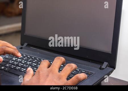 Travail à domicile - les mains de l'homme utilisant un ordinateur portable avec écran sur le bureau à l'intérieur de la maison. Image de style maquette d'une main utilisant et touchant un ordinateur portable sur la table du hom Banque D'Images