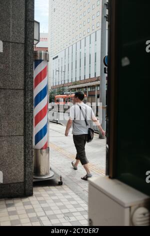 MATSUYAMA, JAPON - 21 septembre 2019 : photo verticale d'une personne marchant près du poteau de barber sur un trottoir Banque D'Images