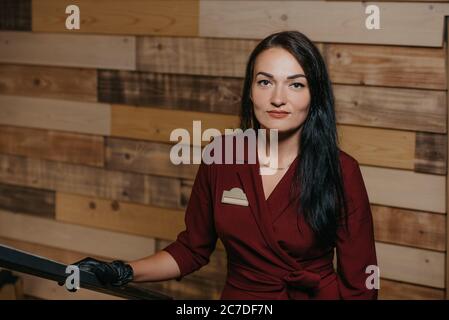 Une photo rapprochée d'une magnifique femme directrice de restaurant avec des gants jetables noirs qui pose dans un café. Un propriétaire de café aimable dans une robe rubis est Banque D'Images