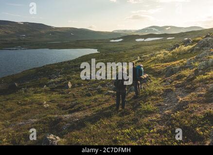 Photo large de deux personnes se tenant près du lac entouré par de belles montagnes sous ciel nuageux Banque D'Images