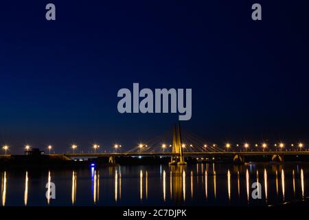 Gros plan d'un pont au-dessus de l'eau avec le réflexion de lumières sous le beau ciel nocturne Banque D'Images