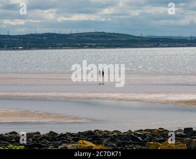 Firth of Forth, East Lothian, Écosse, Royaume-Uni, 16 juillet 2020. Météo britannique : soleil chaud le long de la côte du Forth. Deux personnes apprécient l'eau fraîche seule sur la plage sous le soleil brumeux tandis que la marée recule Banque D'Images