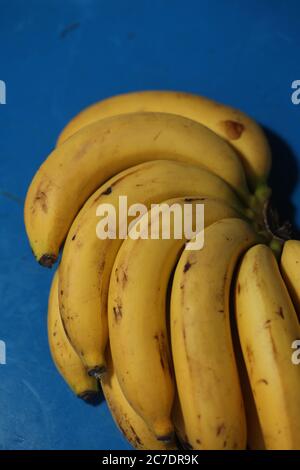 Gros plan vertical d'une main de banane avec des bananes jaunes mûres sur une table bleue Banque D'Images