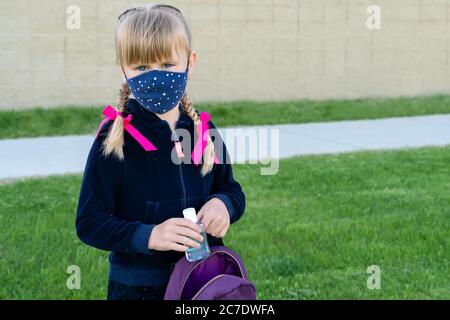 Jeune fille caucasienne portant un masque de protection en coton pour l'école et portant un désinfectant pour les mains. Retour à l'école, réouverture, Banque D'Images