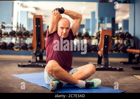 Un portrait d'homme âgé chauve qui s'étire après l'entraînement dans la salle de gym. Concept de personnes, de soins de santé et de mode de vie Banque D'Images