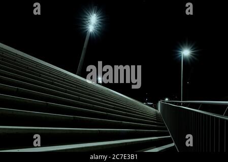 Plan nocturne à angle bas des escaliers avec une main courante en haut et deux grands lampadaires tournés. Banque D'Images