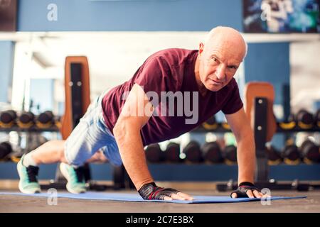 Un portrait d'homme âgé chauve faisant des exercices de poussettes dans la salle de gym. Concept de personnes, de soins de santé et de mode de vie Banque D'Images