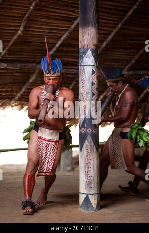 Un indigène amazonien portant une coiffe à plumes et de la peinture faciale joue un instrument cérémoniel, célébrant les traditions culturelles du Brésil. Banque D'Images