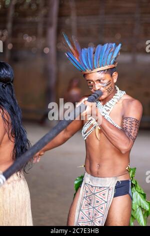 Un indigène amazonien portant une coiffe à plumes et de la peinture faciale joue un instrument cérémoniel, célébrant les traditions culturelles du Brésil. Banque D'Images