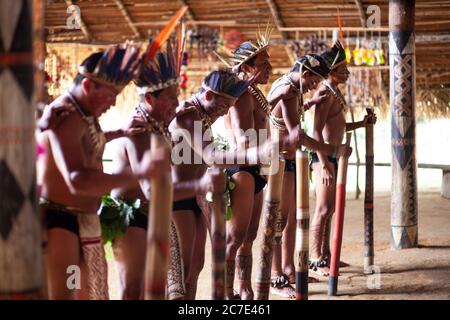 Les hommes indigènes amazoniens exécutent une cérémonie tribale traditionnelle avec des bâtons de cérémonie, portant des coiffes à plumes et de la peinture corporelle, célébrant leur cérémonie Banque D'Images