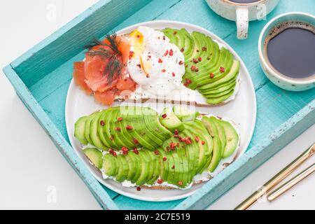 Bruschetta au saumon salé, avocat haché, poivre et œuf poché sur une assiette blanche sur fond de turqoise Banque D'Images