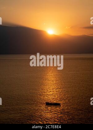Coucher de soleil derrière les montagnes, reflet sur la mer avec petit bateau en premier plan Banque D'Images