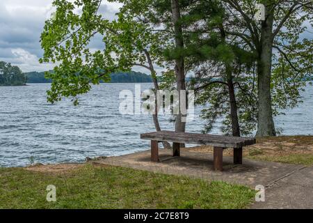 Banc en bois vide assis au bord du lac avec des arbres en arrière-plan, sur une journée nuageux et couvert en été Banque D'Images