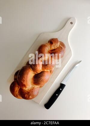 Plan vertical à angle élevé de challah sur un hacher blanc planche à côté d'un couteau sur une surface blanche Banque D'Images