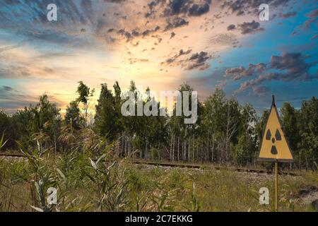 Panneau d'avertissement jaune indiquant le rayonnement dans la zone d'exclusion de tchernobyl, forêt rouge dangereuse en arrière-plan. Fin d'après-midi, beaux soleil dorés Banque D'Images