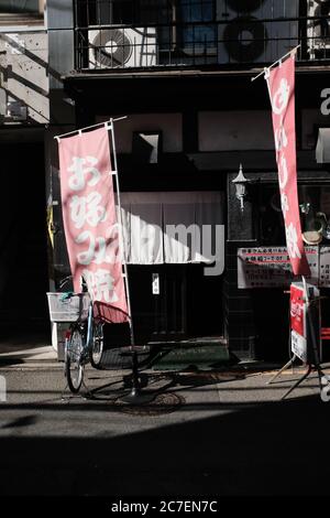 MATSUYAMA, JAPON - 23 septembre 2019 : une photo verticale d'affiches rouges suspendues et d'un vélo devant un ancien bâtiment Banque D'Images