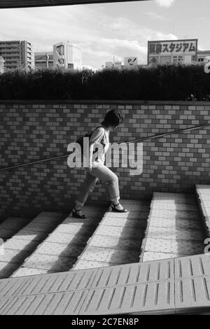 MATSUYAMA, JAPON - 24 septembre 2019 : photo verticale en niveaux de gris d'une femme solitaire qui marche dans les escaliers Banque D'Images