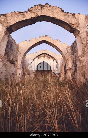 Plan vertical d'une ancienne ruine avec une arche plafond dans un champ herbacé sec sous un ciel bleu Banque D'Images