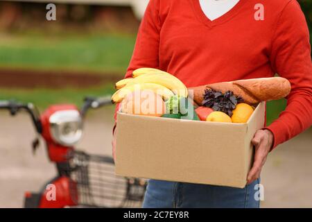 Livreurs de nourriture en uniforme rouge avec une boîte corton avec des provisions dans ses mains Banque D'Images