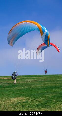 Plan vertical de deux personnes atterrissant avec des parachutes colorés un champ herbacé Banque D'Images