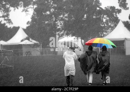 Plan horizontal de trois personnes avec imperméable un sombre et un parapluie de couleur arc-en-ciel Banque D'Images