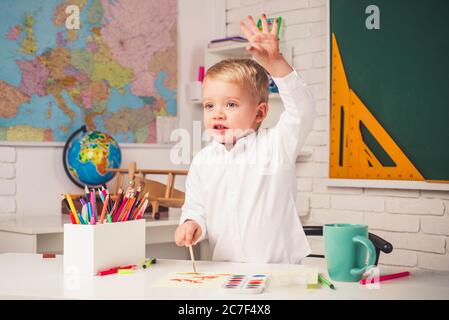 Joyeux mignon enfant industriel est assis à un bureau à l'intérieur. Retour à l'école. Enseignement à domicile. Enfant talentueux. L'enfant se prépare à l'école. Banque D'Images