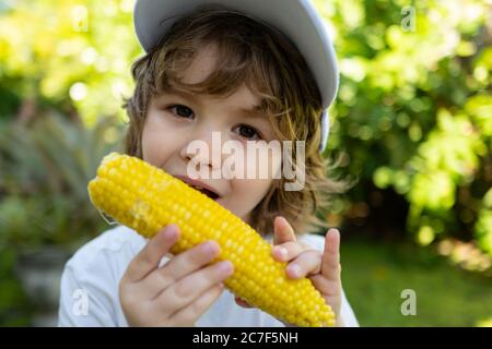 Style de vie d'automne. Aliments biologiques maison. Nutrition des enfants végétaliens. Petit garçon mangeant du maïs en épi. Banque D'Images