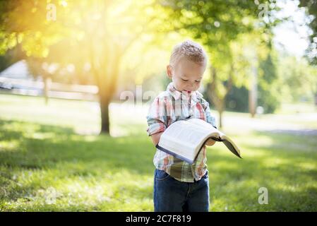 Gros plan d'un enfant tenant une Bible ouverte pendant en regardant avec un arrière-plan flou Banque D'Images