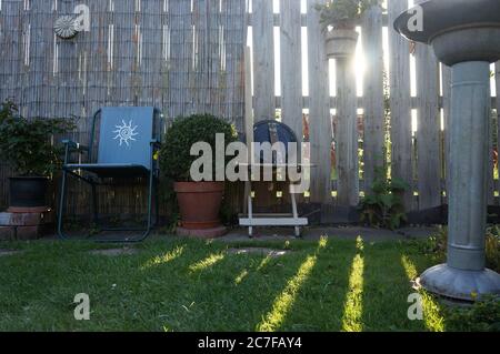 Mobilier de jardin avec le soleil brille à travers une clôture en bois causant des ombres rayées un soir d'été Banque D'Images