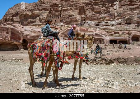 Les Bédouins attendent avec leurs chameaux pour faire monter les touristes à travers les ruines antiques de Pétra en Jordanie. En arrière-plan se trouvent des bâtiments anciens de grottes. Banque D'Images